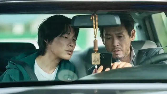 Two men inside a car lean in closely to look at a smartphone screen held by the driver.